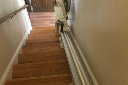 A stairlift installed along a wooden staircase providing assistance for individuals to move between floors.