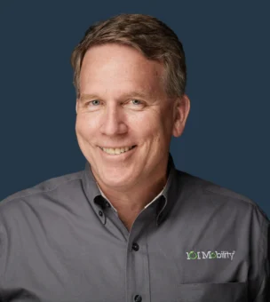 A man wearing a gray shirt with the logo "101 Mobility" smiles at the camera against a dark blue background.