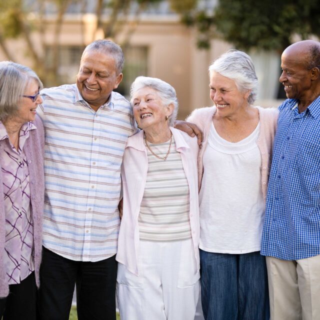 Smiling senior friends standing with arms around.