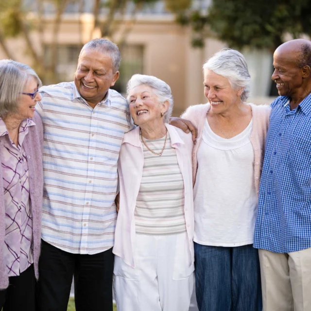 Smiling senior friends standing with arms around.
