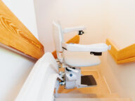 A stairlift installed on a staircase with wooden handrails, designed to assist individuals in navigating stairs.