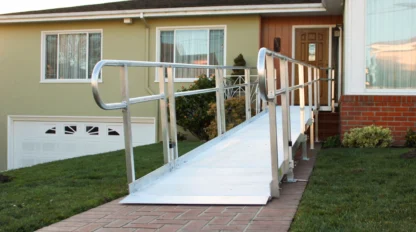 Aluminum wheelchair ramp leading to the front door of a single-story house with a green exterior and brick steps.