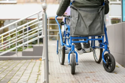 Person in a wheelchair using an outdoor ramp with metal handrails.