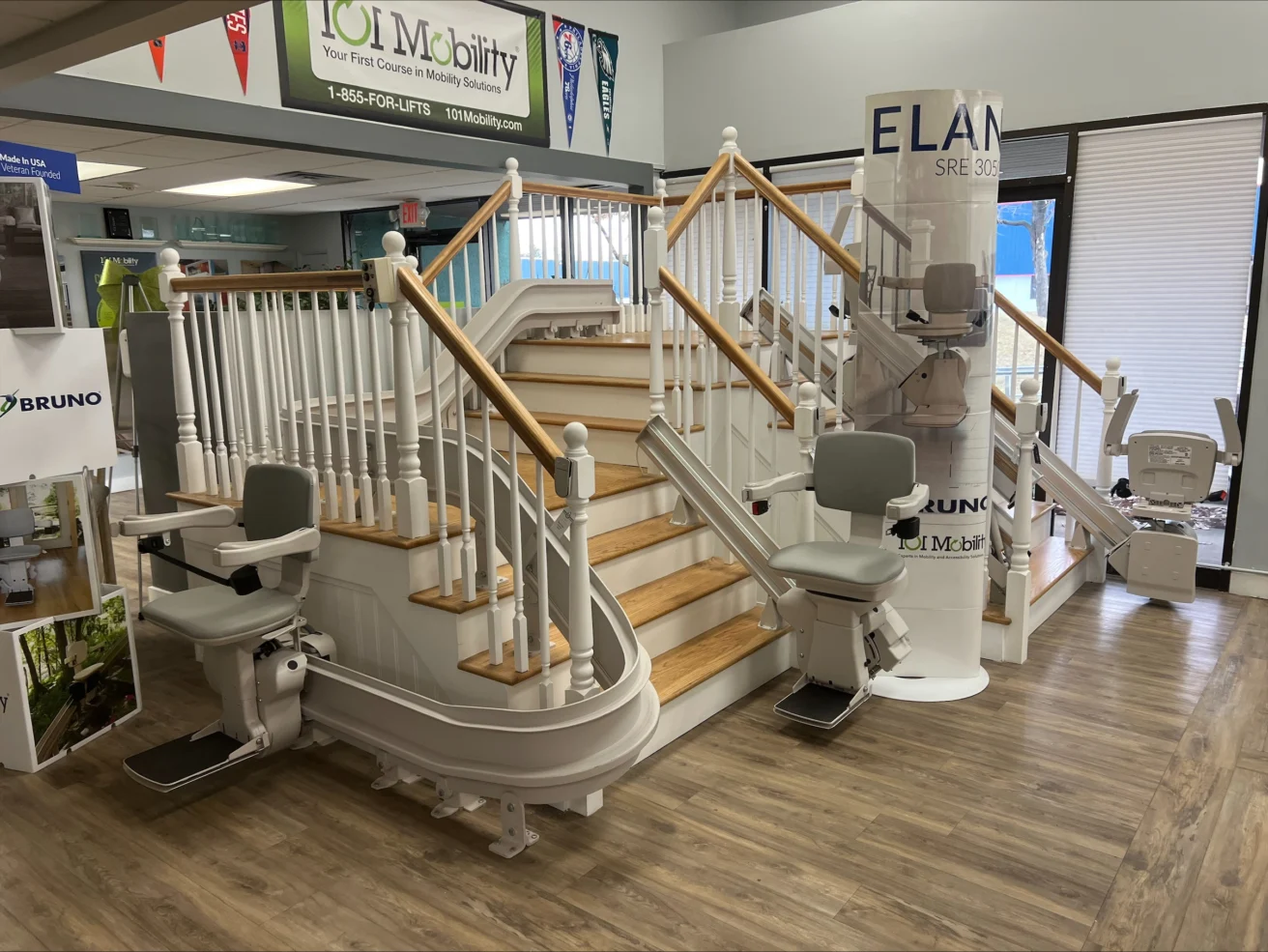 Showroom display of stairlifts, featuring a staircase with multiple models positioned along the railing. Banners and promotional materials are visible in the background.