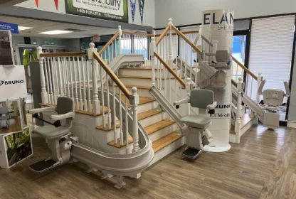 Showroom display of stairlifts, featuring a staircase with multiple models positioned along the railing. Banners and promotional materials are visible in the background.