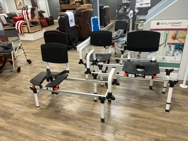 Shower bench seats with adjustable frames displayed in a store. The background includes various furniture items and a banner with product information.
