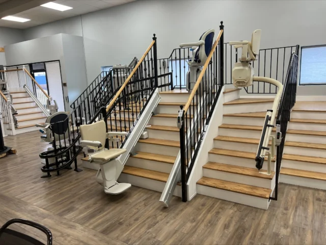 Showroom displaying various stair lifts on wooden staircases with handrails.