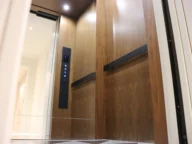 A modern elevator interior with wooden paneling, black handrails, and a control panel with buttons.