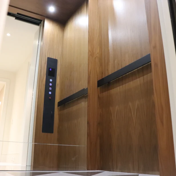 A modern elevator interior with wooden paneling, black handrails, and a control panel with buttons.