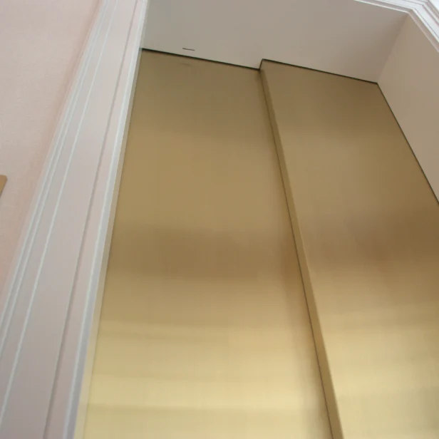Closed gold elevator doors with a beige wall and a button panel on the left.