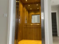 Open wooden-finish elevator with recessed lighting, visible door frame, and partially visible adjacent room entryway.