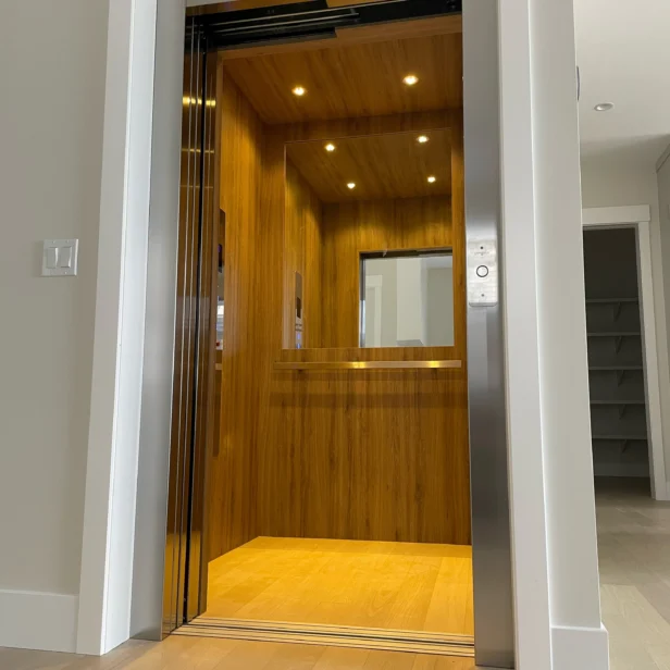 Open wooden-finish elevator with recessed lighting, visible door frame, and partially visible adjacent room entryway.