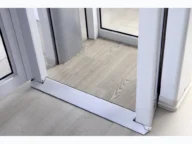 Revolving door with a wooden floor mat and metal frame, positioned on a light tiled floor.