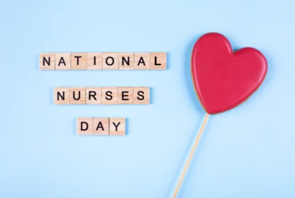 Scrabble tiles spell "National Nurses Day" next to a red heart-shaped object on a stick, all set against a light blue background.