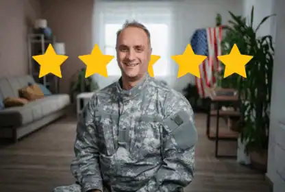A man in military uniform sits and smiles in a living room, with five yellow stars and an American flag visible in the background.