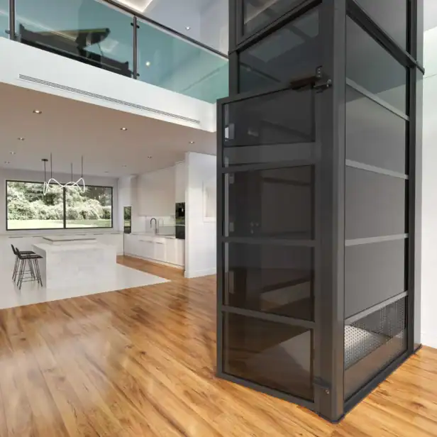 A modern glass residential elevator in a spacious open-plan living area with wood floors, white walls, and a kitchen visible in the background.