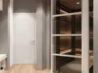 A modern indoor residential elevator with glass doors is next to a white closed door in a room with wood flooring and gray walls.
