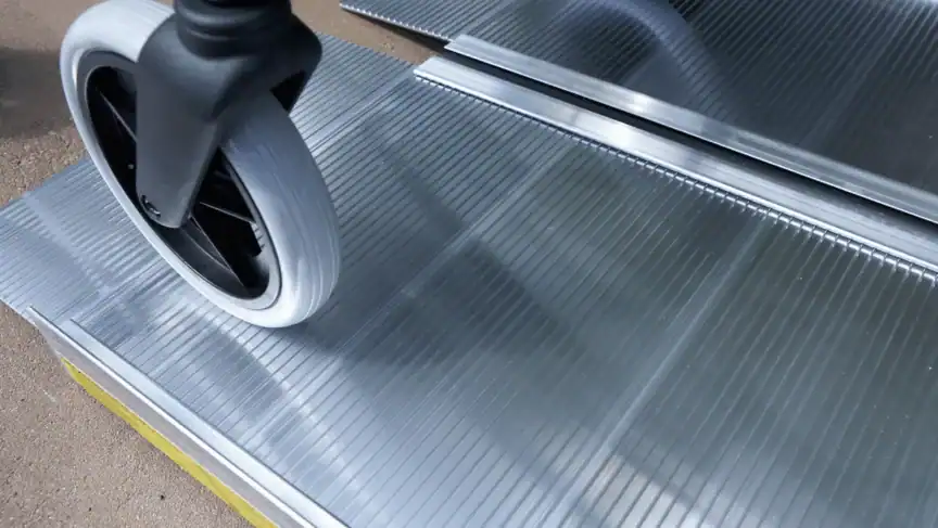 Close-up of a wheelchair wheel moving over a metal ramp with a grooved surface.