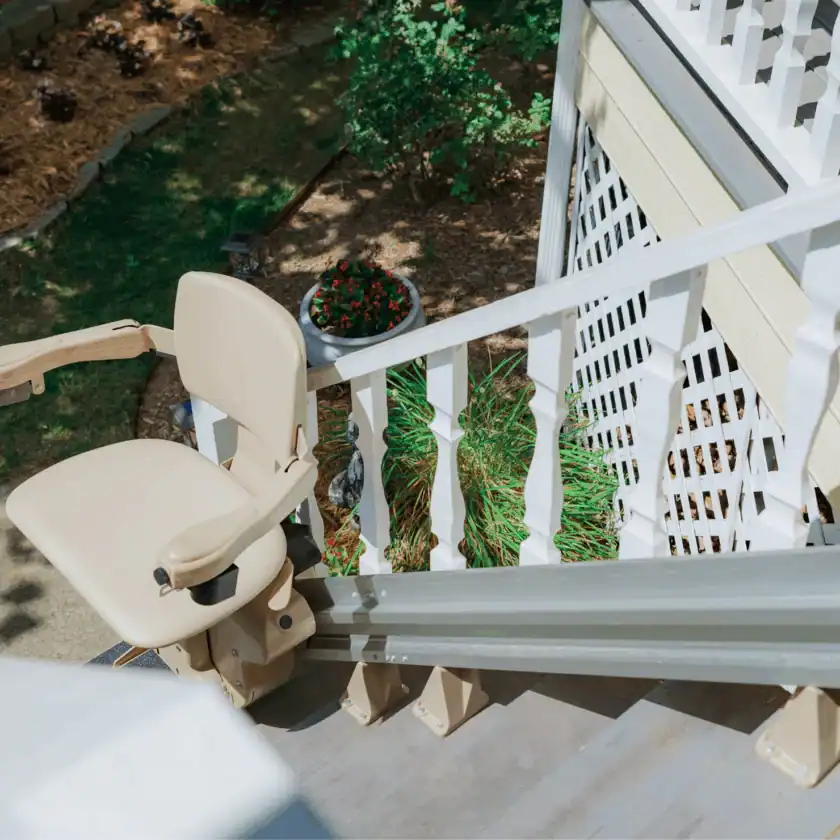 A beige stair lift is installed on the outdoor steps of a house, with a garden visible below.