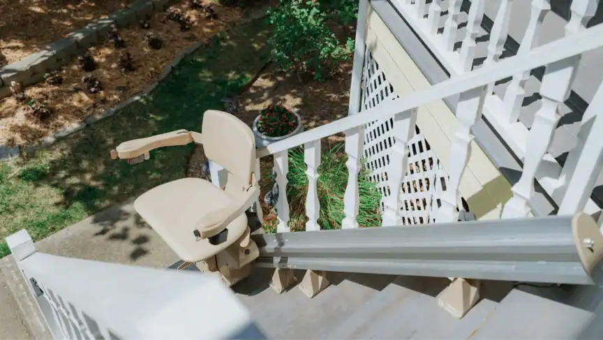 A beige stair lift is installed on the outdoor steps of a house, with a garden visible below.