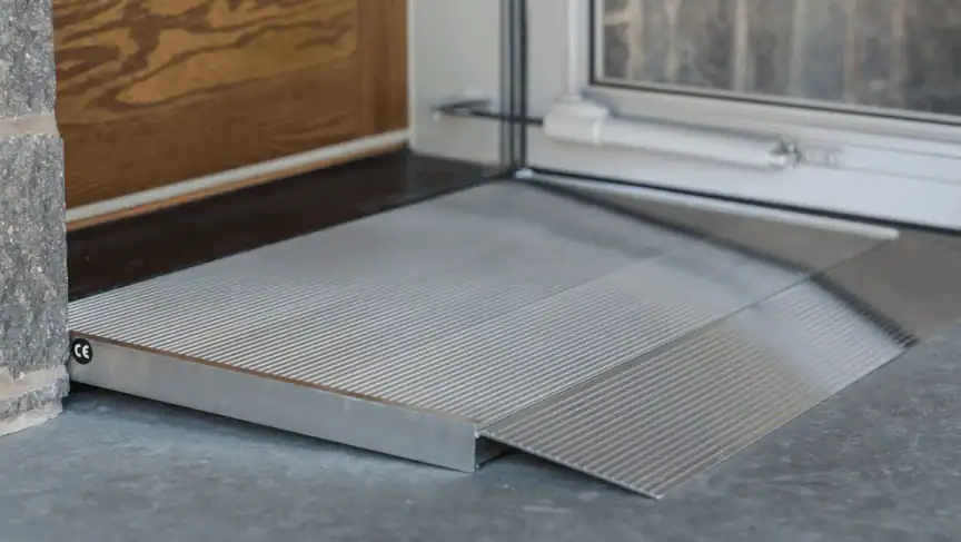 A metal wheelchair ramp with a grooved surface is placed at the entrance of a doorway on a concrete floor, providing accessible entry.