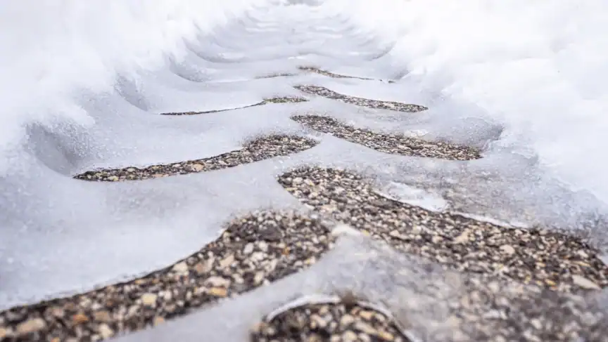 Several human footprints are visible in melting ice on a gravel path, creating a repeating pattern where the ice has thinned over each footprint.