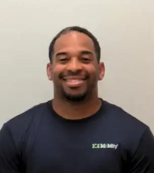 A man wearing a navy blue "101 Mobility" shirt smiles at the camera against a plain light-colored background.