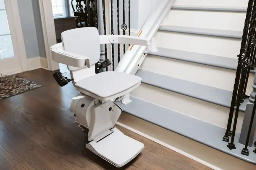 A motorized stairlift chair is installed beside a staircase in a home, designed to assist with mobility between floors.