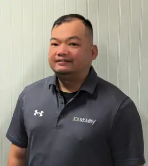 A person with short hair wearing a gray polo shirt with "101 Mobility" and Under Armour logos stands in front of a white, vertically paneled wall.