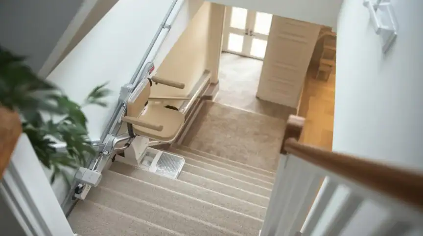 A stairlift is installed along the side of a carpeted staircase in a home, providing accessibility between floors.