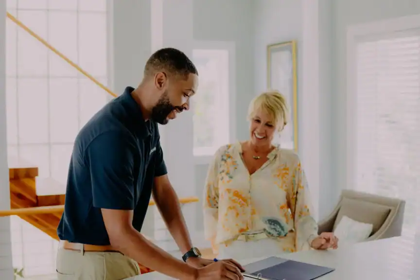 A man shows documents to two women at a table in a bright room.