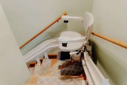 A motorized stair lift chair is installed along a staircase with handrails and patterned rugs on the steps.