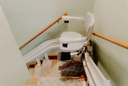 A motorized stair lift chair is installed along a staircase with handrails and patterned rugs on the steps.