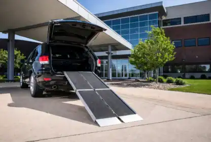 An SUV with its rear door open and a portable ramp extended to the ground, positioned outside a modern office building.