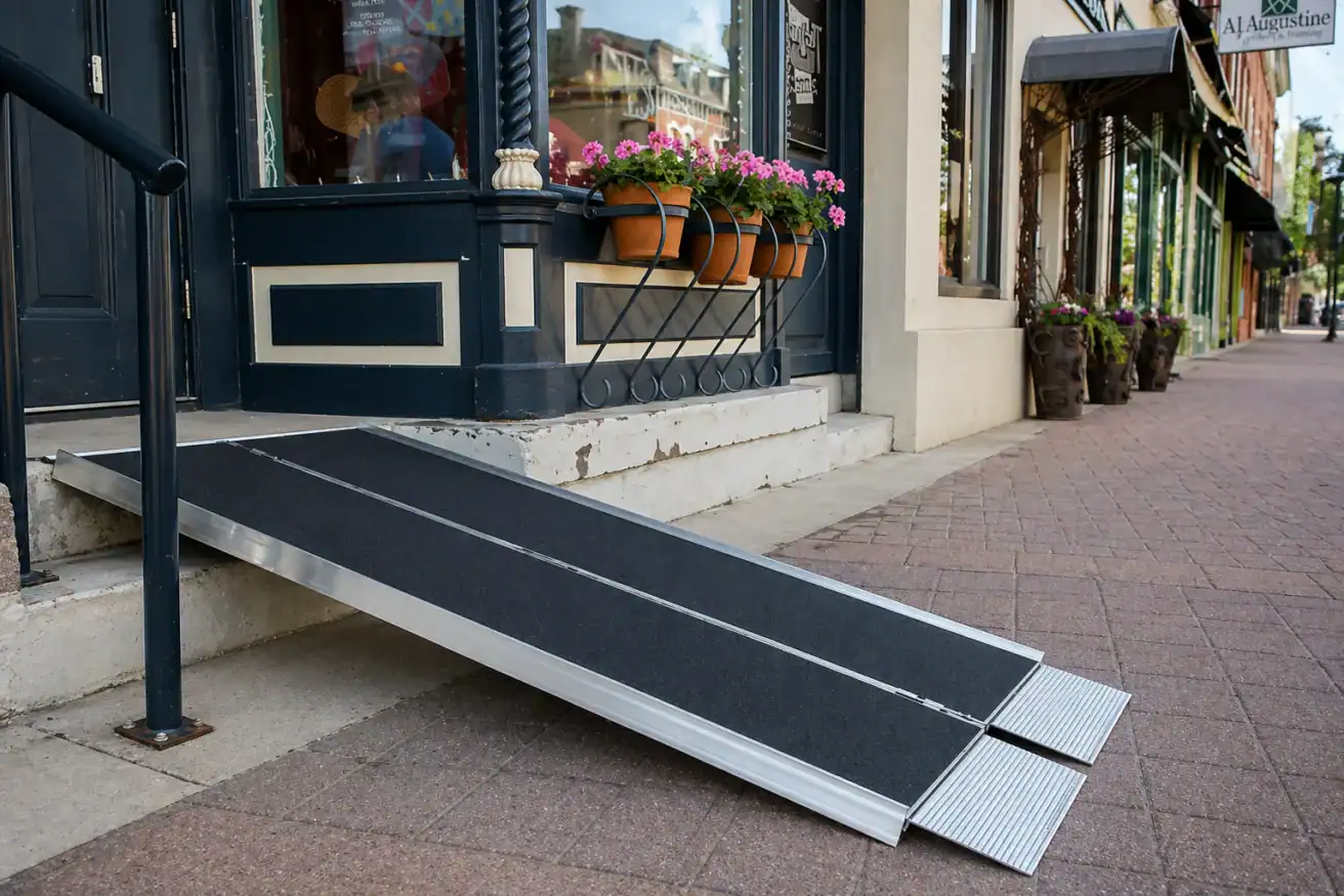 A portable wheelchair ramp is placed over steps at the entrance of a storefront, providing accessible entry from the sidewalk.
