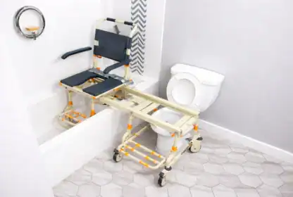 A transfer bench with wheels bridges a bathtub and a toilet in an accessible bathroom, facilitating safe movement for individuals with mobility needs.