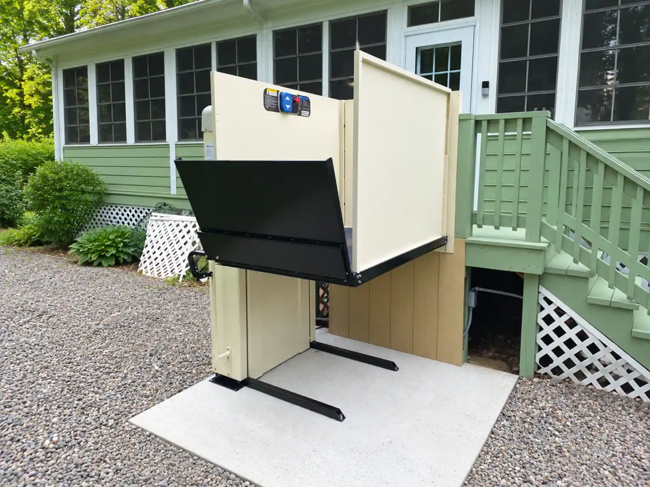 An outdoor vertical platform lift installed on a concrete pad next to a house deck.