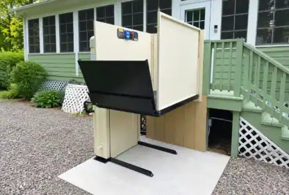 An outdoor vertical platform lift installed on a concrete pad next to a house deck.