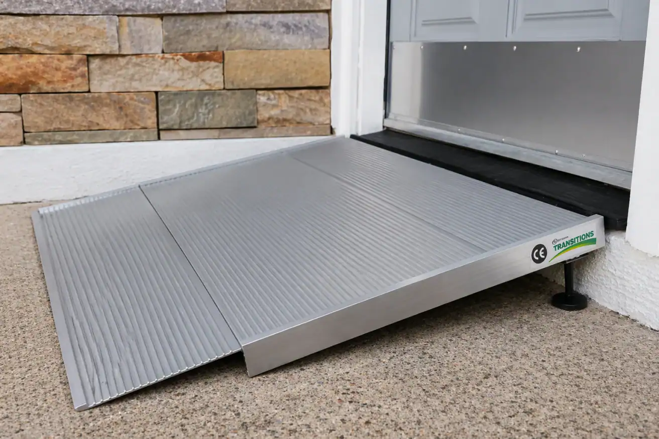 A portable aluminum wheelchair ramp is positioned at a doorway, providing accessible entry over a raised threshold.