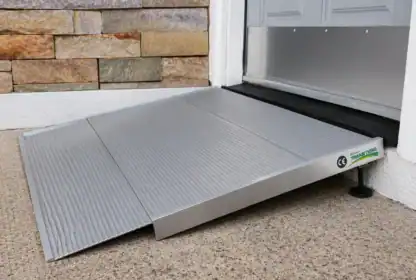 A portable aluminum wheelchair ramp is positioned at a doorway, providing accessible entry over a raised threshold.