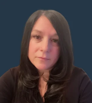 A woman with long dark hair and a neutral expression poses against a solid dark blue background.