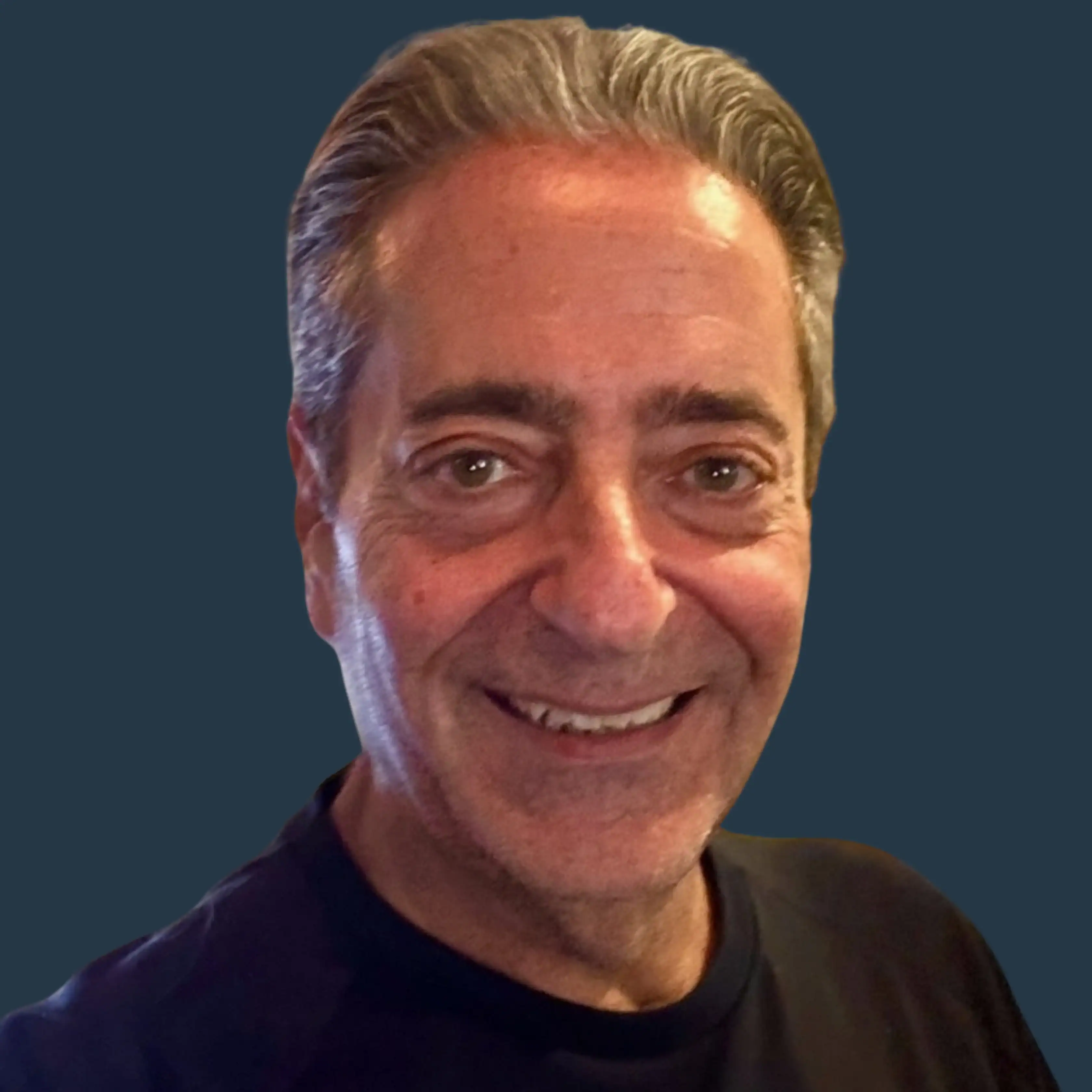 Smiling middle-aged man with short gray hair wearing a black shirt, shown against a plain dark background.