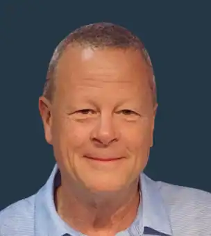 A middle-aged man with short hair, wearing a light blue collared shirt, smiles in front of a solid dark background.