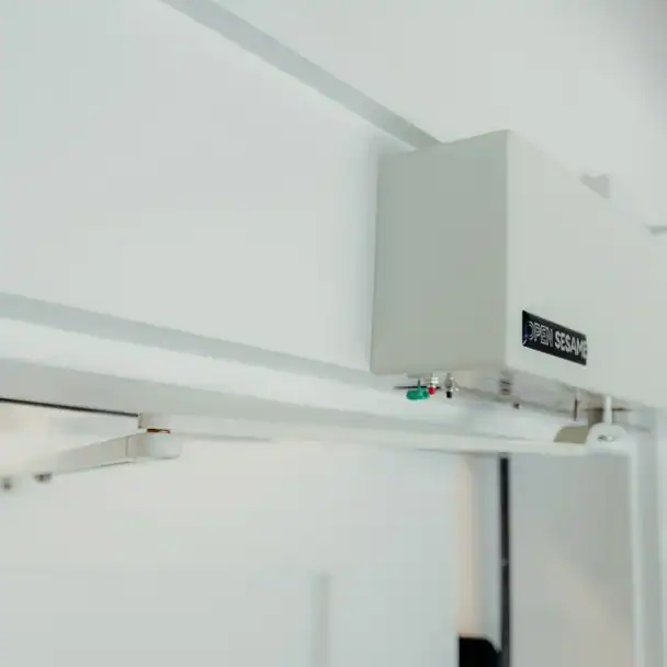 Close-up of an automatic door opener device labeled "Open Sesame" installed on a white doorframe.