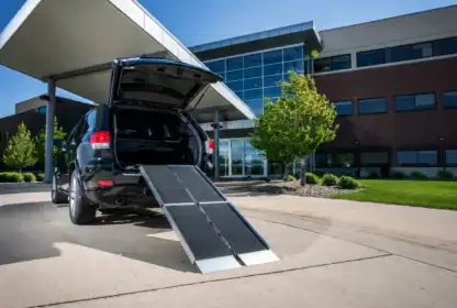 A black SUV with its trunk open and a wheelchair ramp extended onto a sidewalk outside a modern building.