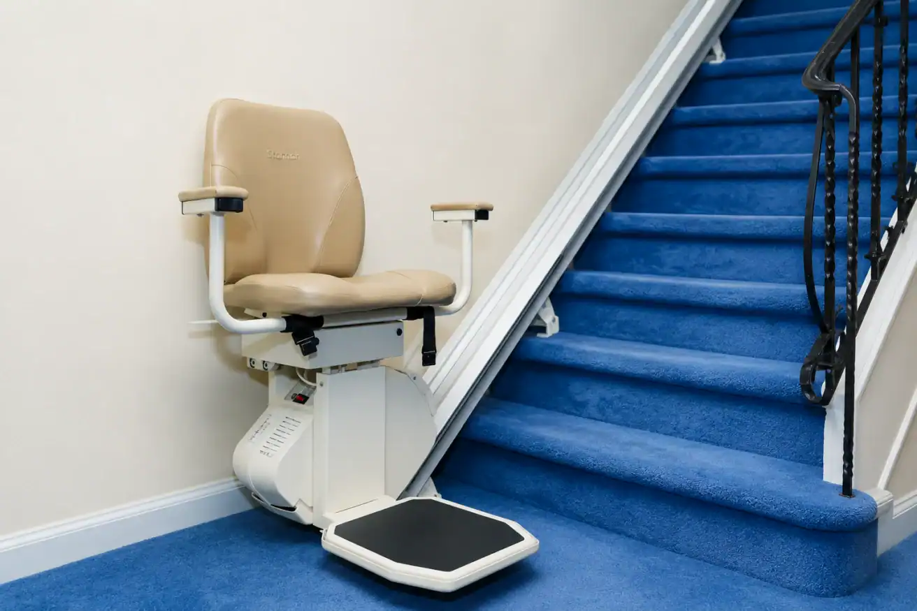 A beige stairlift chair is installed next to a staircase with bright blue carpet and a black handrail.