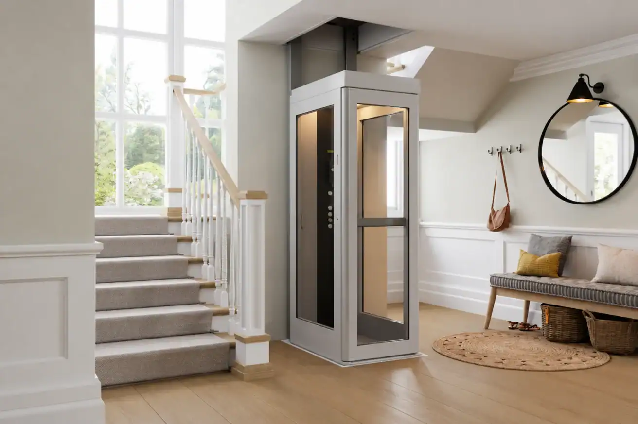 A modern home interior with a small residential elevator next to a carpeted staircase, a bench, round mirror, and large windows letting in natural light.