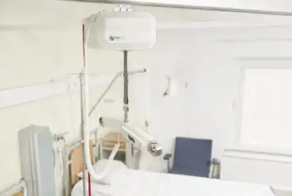 Ceiling-mounted patient lift system installed above a hospital bed in a brightly lit, unoccupied hospital room.