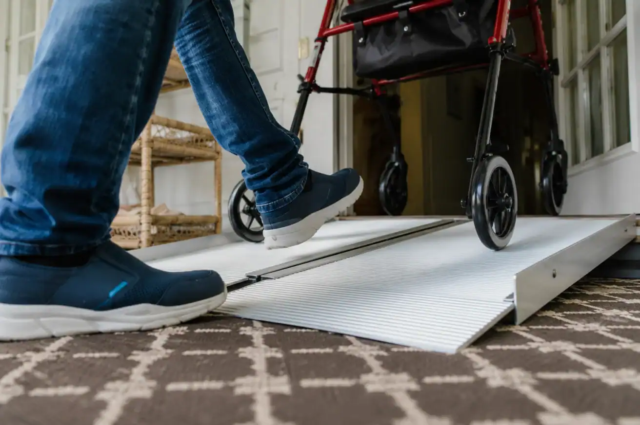 A person steps up a wheelchair ramp next to a red walker inside a home.