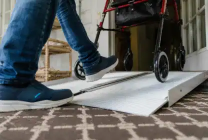A person steps up a wheelchair ramp next to a red walker inside a home.